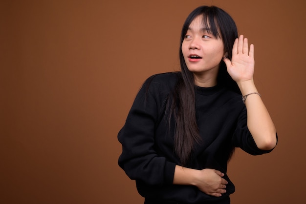 Joven hermosa mujer asiática con suéter negro contra marrón