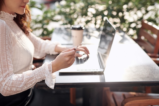 Joven hermosa mujer asiática con tarjeta de crédito y computadora portátil para compras en línea en la cafetería al aire libre