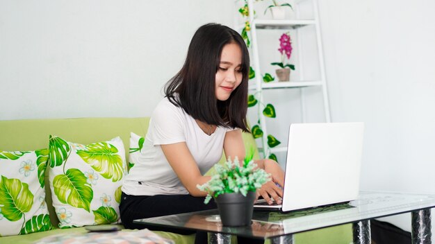 Joven hermosa mujer asiática trabajando desde casa usando la computadora portátil y sentado en una silla