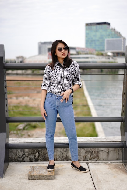 Joven hermosa mujer asiática vestida con camisa a cuadros y pantalones vaqueros azules posando al aire libre