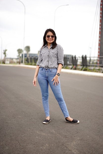 Joven hermosa mujer asiática vestida con camisa a cuadros y pantalones vaqueros azules posando al aire libre