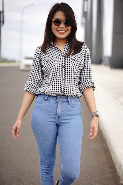 Joven hermosa mujer asiática vestida con camisa a cuadros y pantalones vaqueros azules posando al aire libre