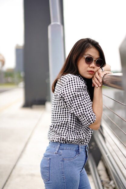 Joven hermosa mujer asiática vestida con camisa a cuadros y pantalones vaqueros azules posando al aire libre