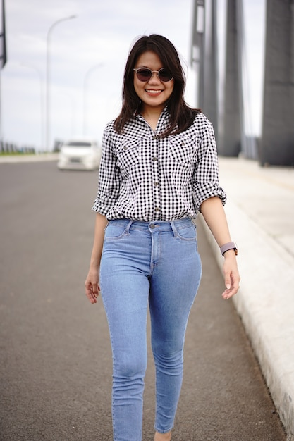 Joven hermosa mujer asiática vestida con camisa a cuadros y pantalones vaqueros azules posando al aire libre