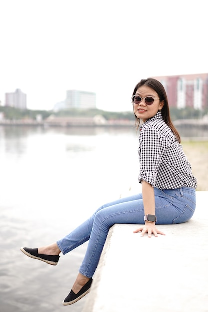 Joven hermosa mujer asiática vestida con camisa a cuadros y pantalones vaqueros azules posando al aire libre