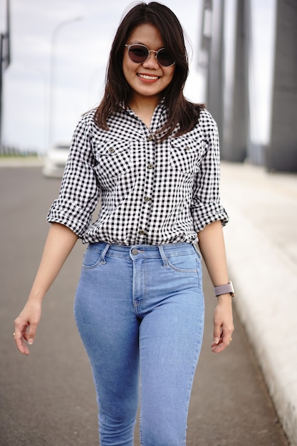 Joven hermosa mujer asiática vestida con camisa a cuadros y pantalones vaqueros azules posando al aire libre