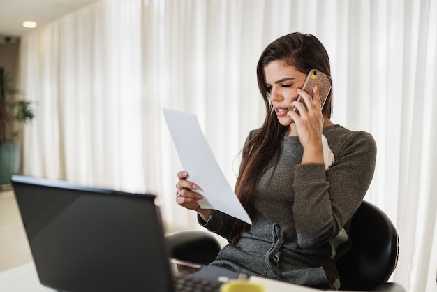 Joven hermosa mujer brasileña con smartphone y trabajando con ordenador portátil