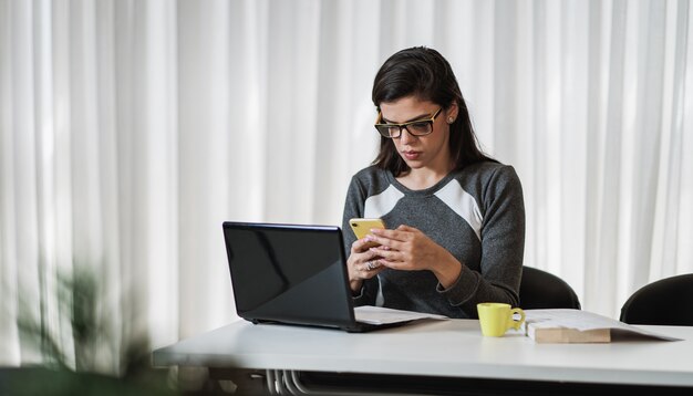 Joven hermosa mujer brasileña con smartphone y trabajando con ordenador portátil