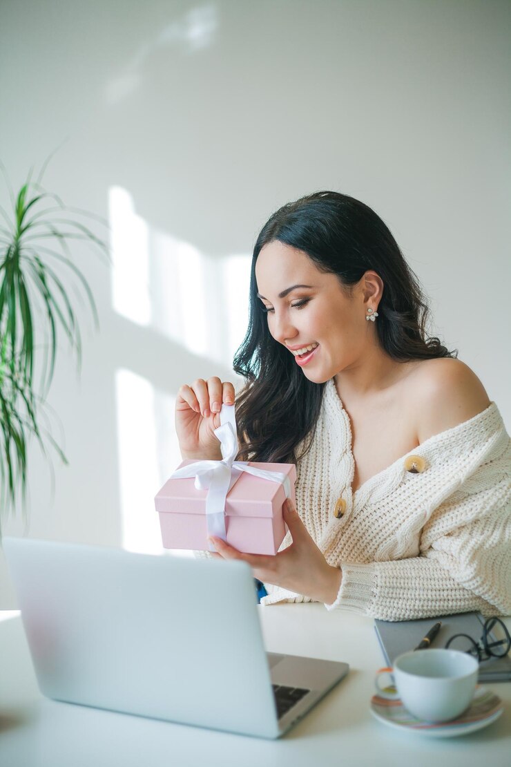 Foto joven hermosa mujer de cabello oscuro de 34 años con suéter de punto está hablando por enlace de video y sosteniendo una caja de regalo rosa en sus manos el modelo del día de san valentín recibió un regalo