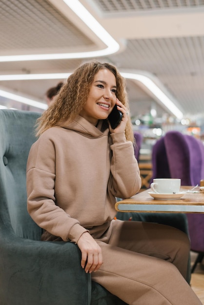 Joven hermosa mujer caucásica hablando por teléfono inteligente en el café