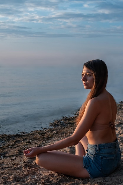 Joven hermosa mujer delgada está haciendo yoga en la orilla del mar en la arena