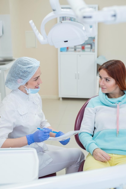 Joven hermosa mujer dentista está hablando con su paciente Mujer pelirroja sonriendo en la recepción del médico Servicios dentales