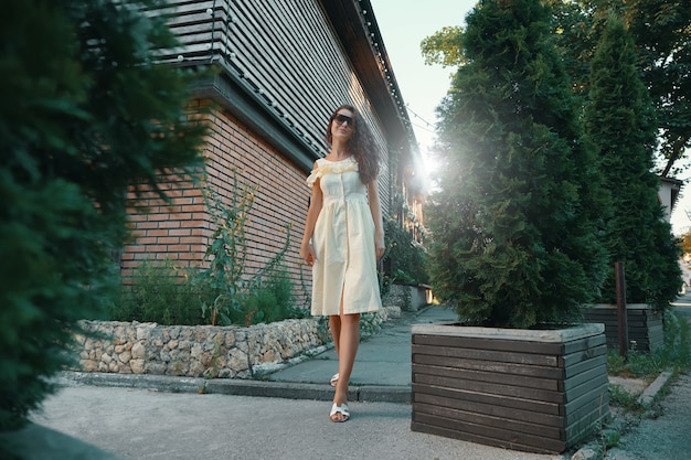 Joven hermosa mujer elegante en gafas de sol caminando sobre un vestido de verano