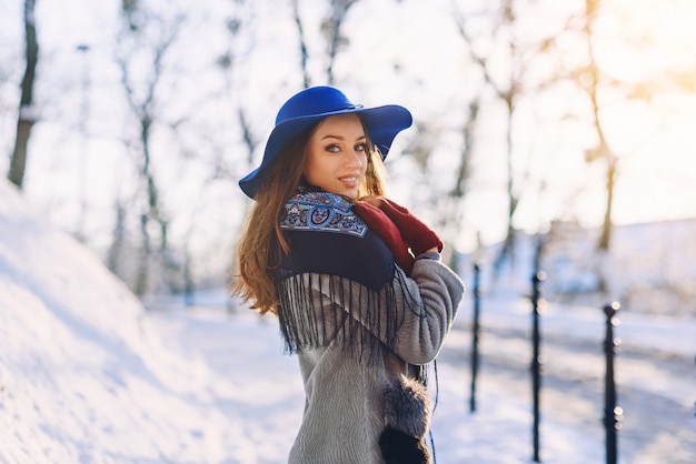 Joven hermosa mujer elegante con una sonrisa perfecta con sombrero azul y bufanda caminando por la calle