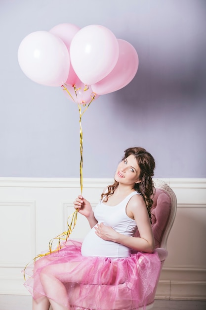 Joven hermosa mujer embarazada con globos de color rosa y una falda de ballet rosa sobre fondo retro