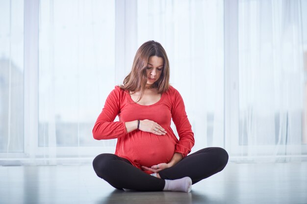 Joven hermosa mujer embarazada haciendo yoga asana Padmasana