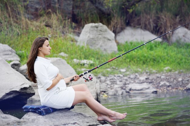 Joven hermosa mujer embarazada pescando en la orilla del río