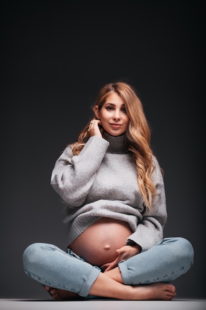 Joven hermosa mujer embarazada sentada en la pared negra