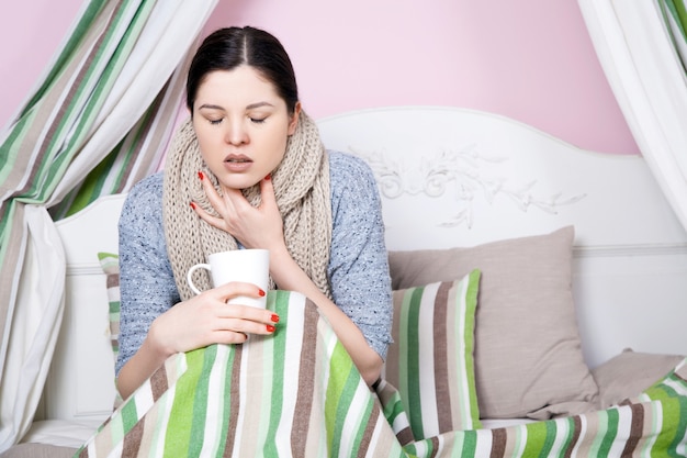 Joven hermosa mujer enferma sintiéndose enferma y mal acostada en la cama sufriendo dolor de cabeza y temperatura tratando de descansar y dormir en la cama.