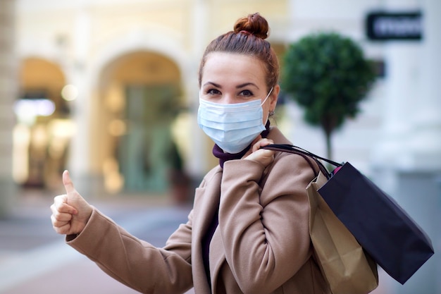 Foto joven hermosa mujer feliz está de compras en el centro comercial, con máscara médica protectora en su rostro