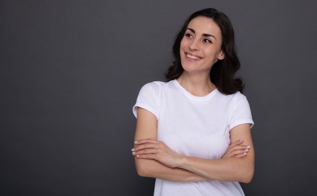 Foto joven hermosa mujer feliz con estilo en una camiseta blanca está posando sobre el fondo gris