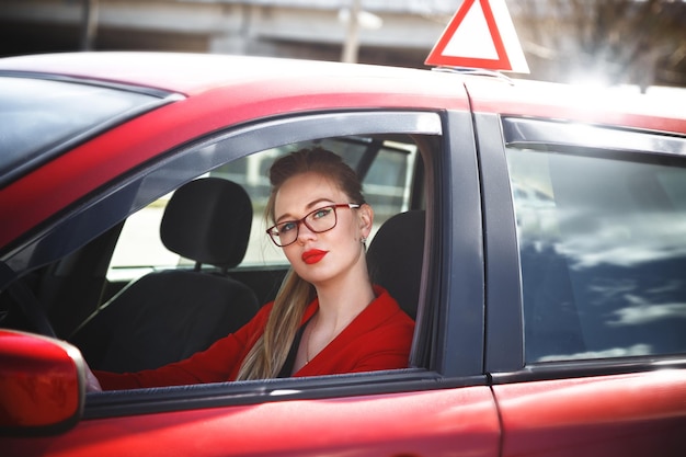 Foto joven hermosa mujer feliz en rojo sentado al volante nuevo coche de entrenamiento.