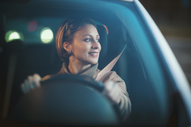 Joven hermosa mujer feliz sentada al volante de un auto nuevo y mirando a través de la ventana del auto.