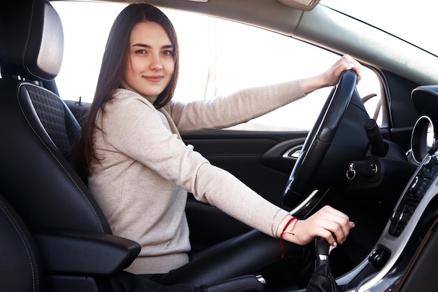 Joven hermosa mujer feliz sentada al volante de un coche nuevo.