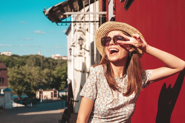 Joven hermosa mujer hipster sonriente en vestido de verano de moda Sexy mujer despreocupada posando en el fondo de la calle cerca de la pared roja en el sombrero al atardecer Modelo positivo al aire libre Alegre y feliz