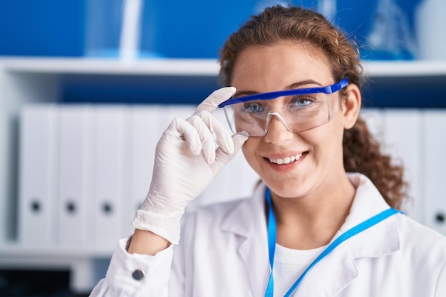 Joven hermosa mujer hispana científica sonriendo segura de pie en el laboratorio