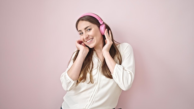 Joven hermosa mujer hispana escuchando música y bailando sobre un fondo rosa aislado