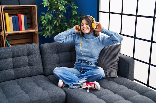 Joven hermosa mujer hispana escuchando música sentada en un sofá en casa