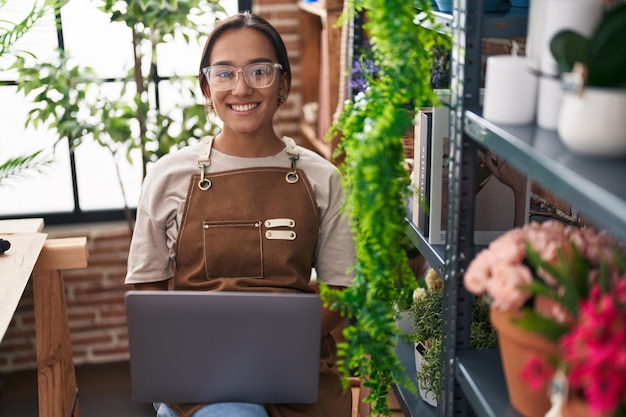 Joven hermosa mujer hispana florista sonriendo confiada usando una computadora portátil en la floristería