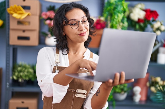 Joven hermosa mujer hispana floristería sonriendo confiada usando una laptop en la floristería