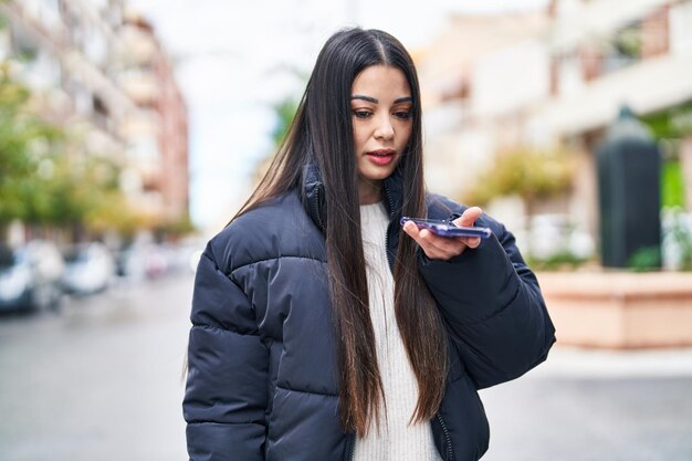 Joven hermosa mujer hispana hablando por teléfono inteligente con expresión relajada en la calle