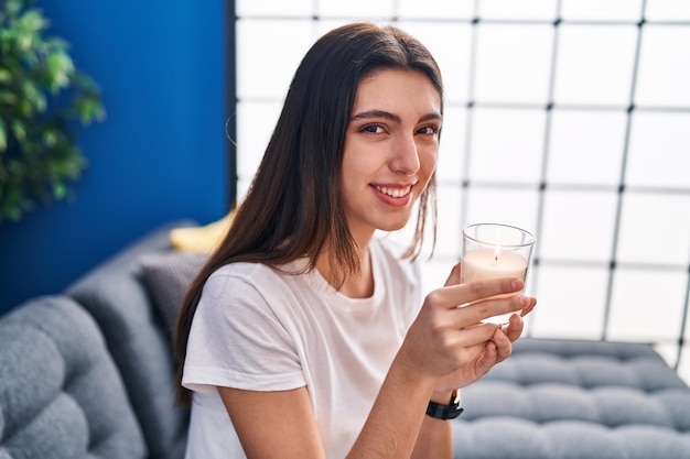 Joven hermosa mujer hispana sentada en un sofá oliendo velas aromáticas en casa