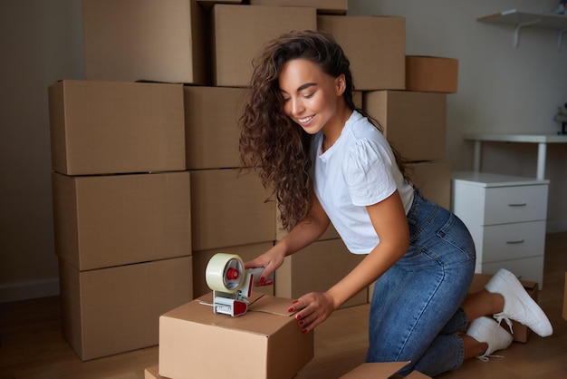 Joven hermosa mujer hispana sonriendo confiada caja de cartón de embalaje en el nuevo hogar