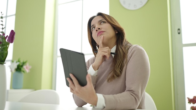 Joven hermosa mujer hispana usando touchpad con expresión de duda en casa