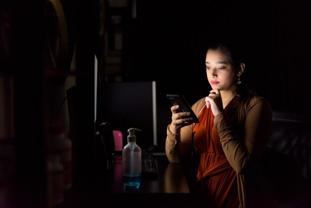 Joven hermosa mujer india pensando mientras usa el teléfono y trabaja desde su casa a altas horas de la noche en la oscuridad