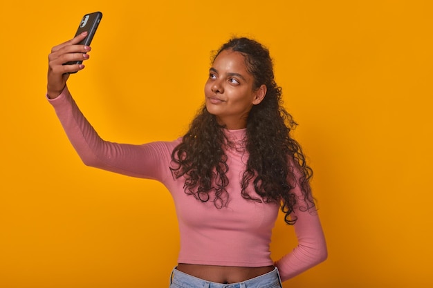 Joven hermosa mujer india sosteniendo el teléfono con los brazos extendidos en el estudio