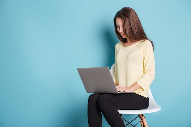 Joven hermosa mujer inteligente con ordenador portátil para estudio aislado sobre fondo azul.