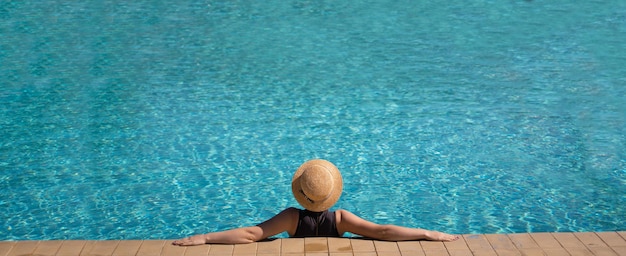 Foto joven hermosa mujer irreconocible en un sombrero de paja está descansando durante unas vacaciones en la pancarta del espacio de copia de la piscina