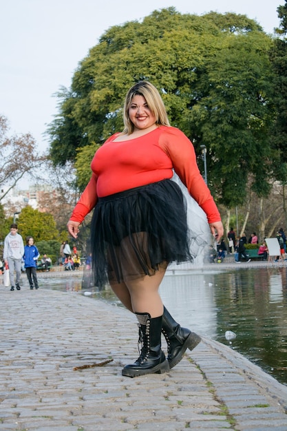 Joven hermosa mujer latina de talla grande posando en el parque con falda  tutú negra y suéter rojo