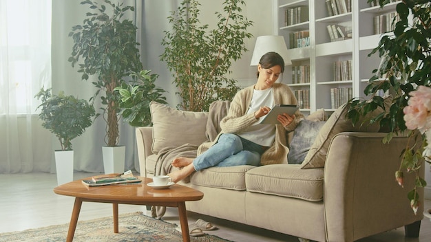 Joven y hermosa mujer mirando su tableta en su apartamento