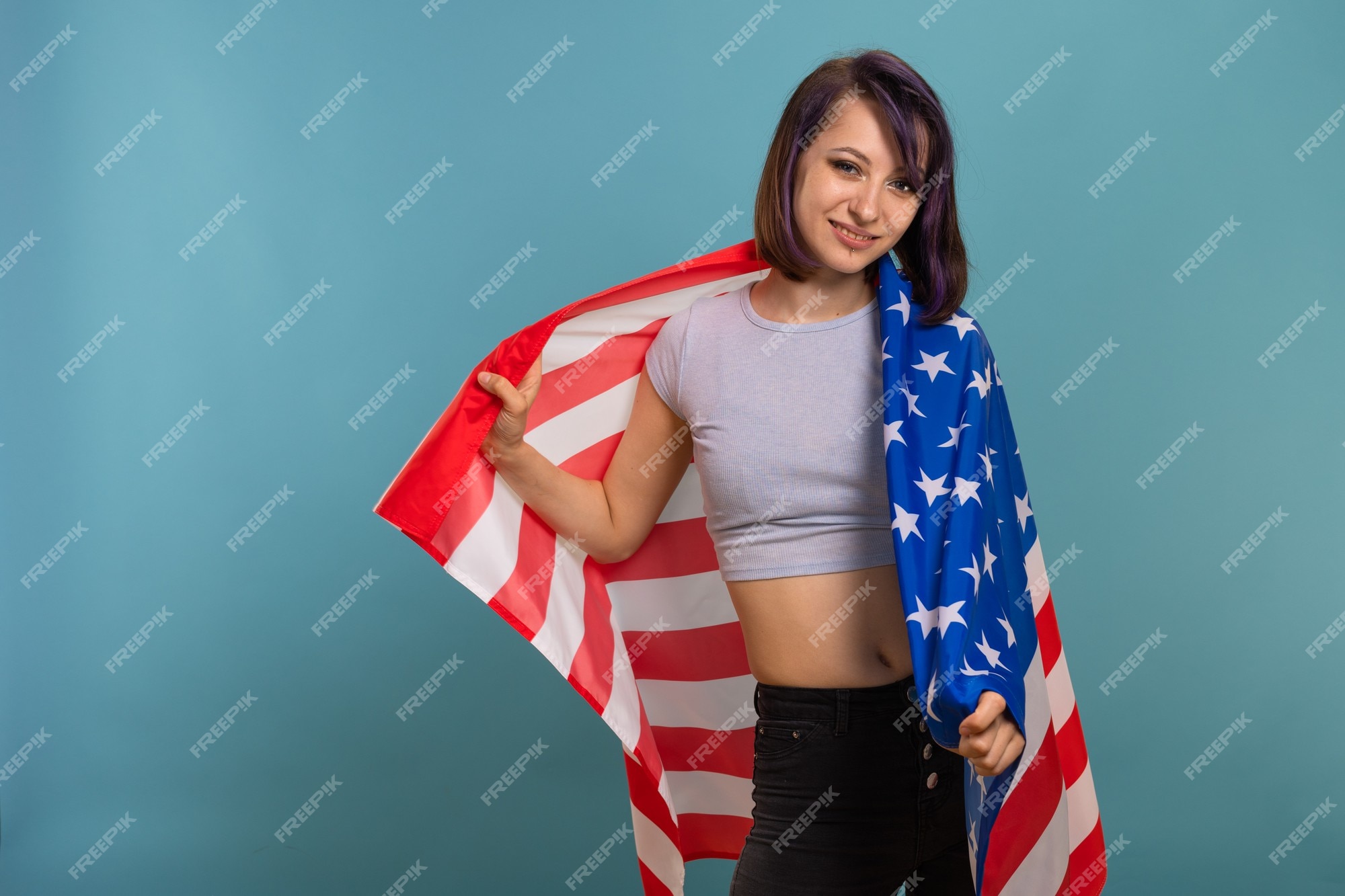 Joven hermosa mujer morena con cabello teñido de púrpura y con la de estados unidos de rayas de estrellas americanas en sus manos un fondo | Foto Premium