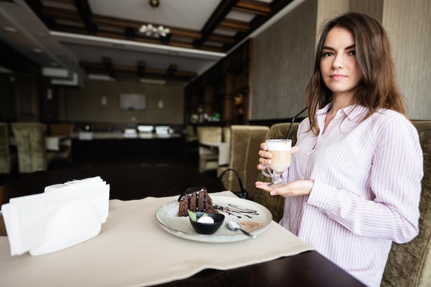 Joven hermosa mujer morena sentada en una cafetería restaurante en el interior y bebiendo café con leche