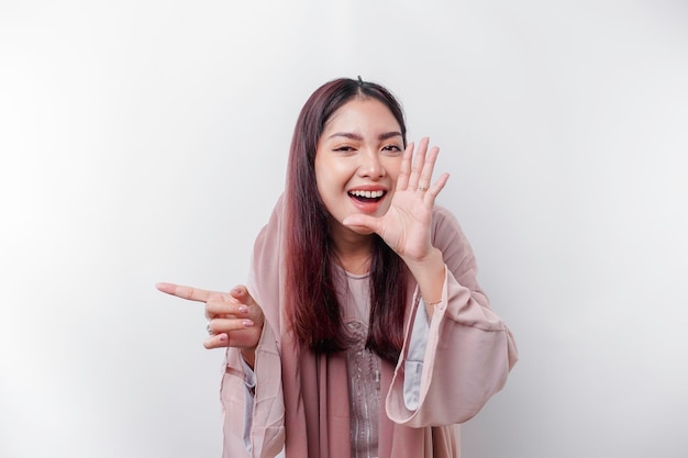 Joven hermosa mujer musulmana asiática con un pañuelo en la cabeza gritando y gritando fuerte con una mano en la boca concepto de comunicación