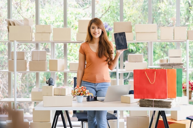 Joven hermosa mujer de negocios asiática feliz está de pie y sosteniendo una tableta