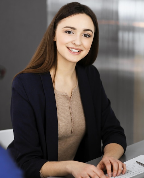 Una joven y hermosa mujer de negocios está hablando con su colega mientras se sienta en el escritorio de una oficina moderna. Concepto de éxito empresarial.