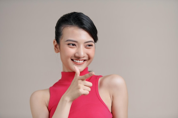 Joven hermosa mujer de negocios morena sonriendo mirando a la cámara apuntando con el dedo hacia adentro sobre un fondo blanco